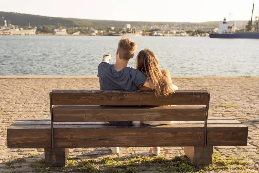 Paar sitzt von hinten auf einer Holzbank am Hafen